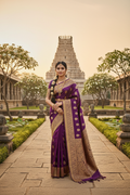 Indian woman wearing a deep purple and gold Kanjivaram silk saree in a temple garden